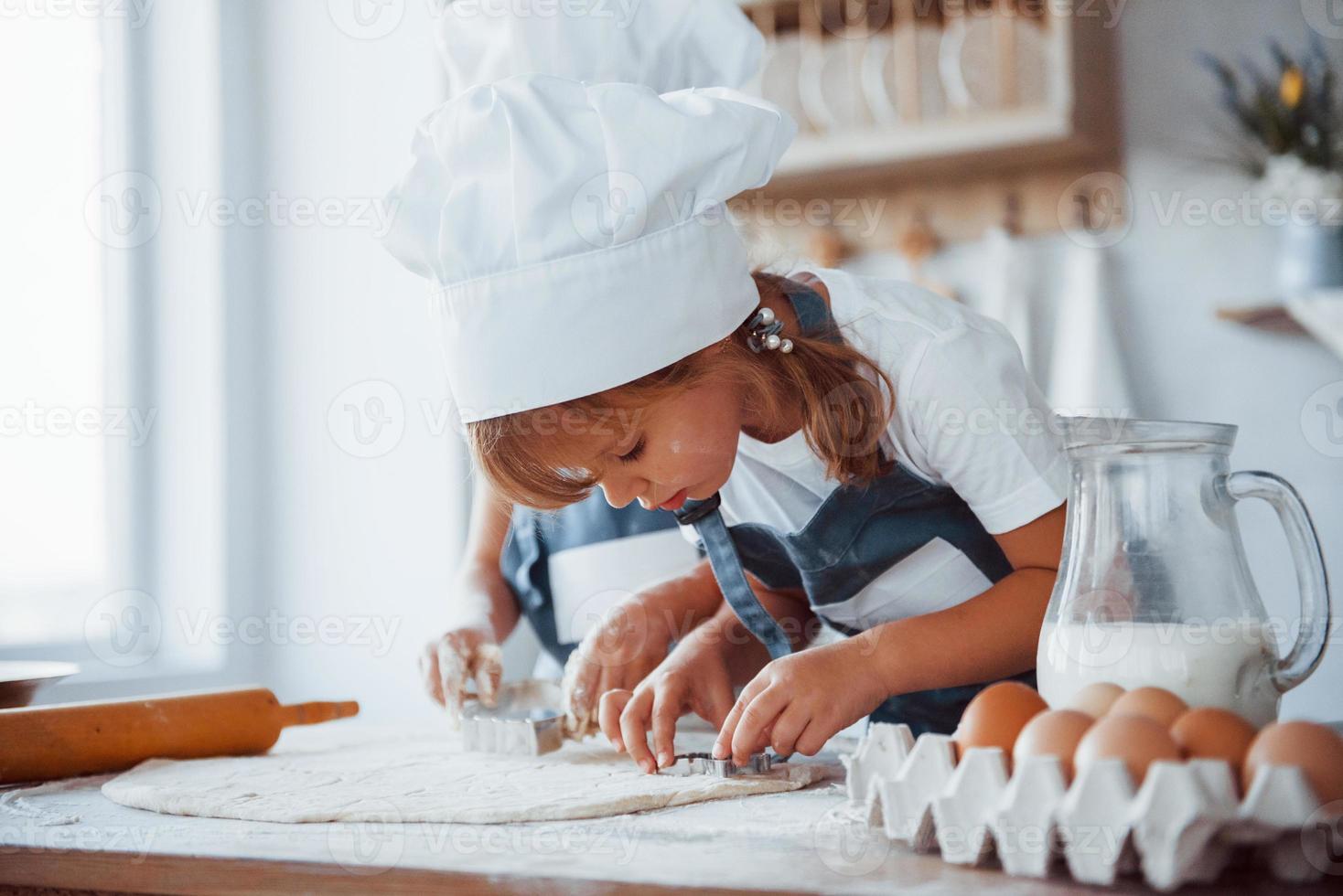 Konzentration aufs Kochen. Familienkinder in weißer Kochuniform bereiten Essen in der Küche zu foto