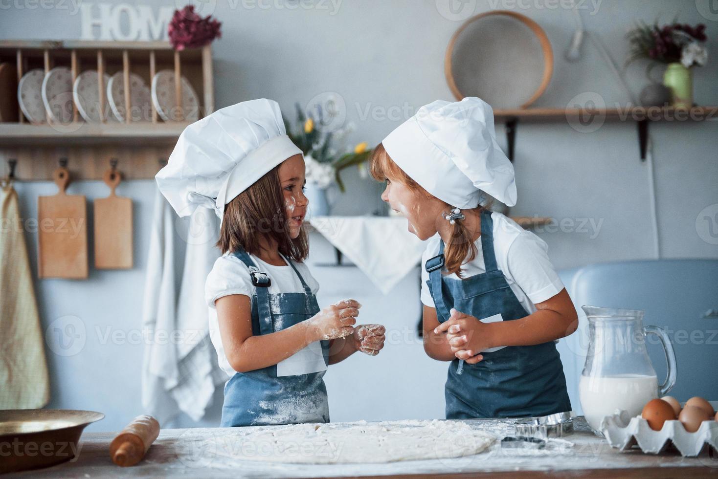 viel Spaß während des Prozesses. Familienkinder in weißer Kochuniform bereiten Essen in der Küche zu foto