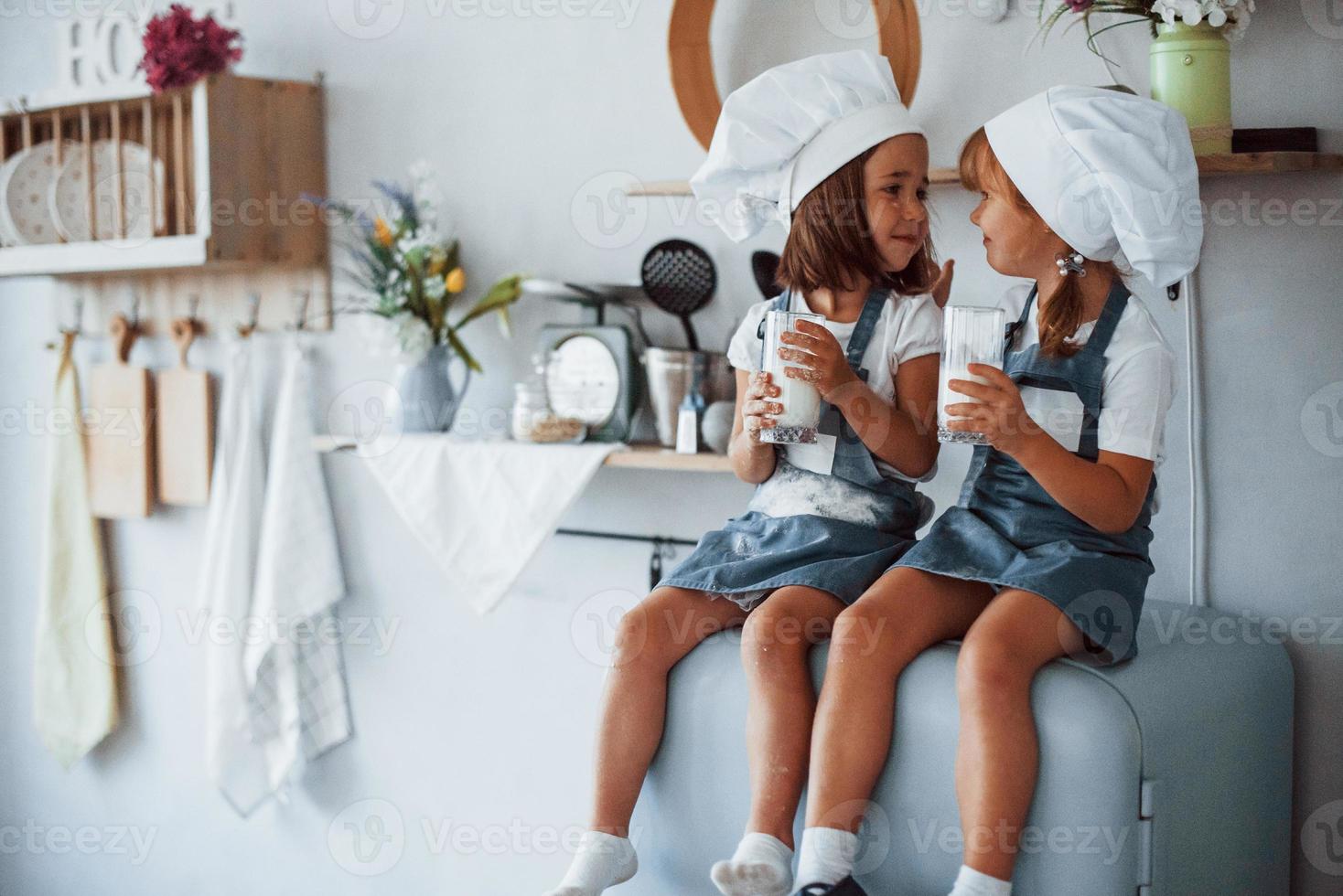 am Kühlschrank sitzen. Familienkinder in weißer Kochuniform essen Essen in der Küche foto