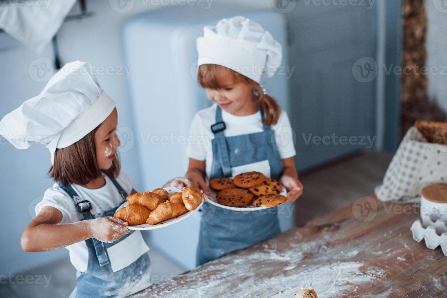 Kekse sind fertig. Familienkinder in weißer Kochuniform bereiten Essen in der Küche zu foto