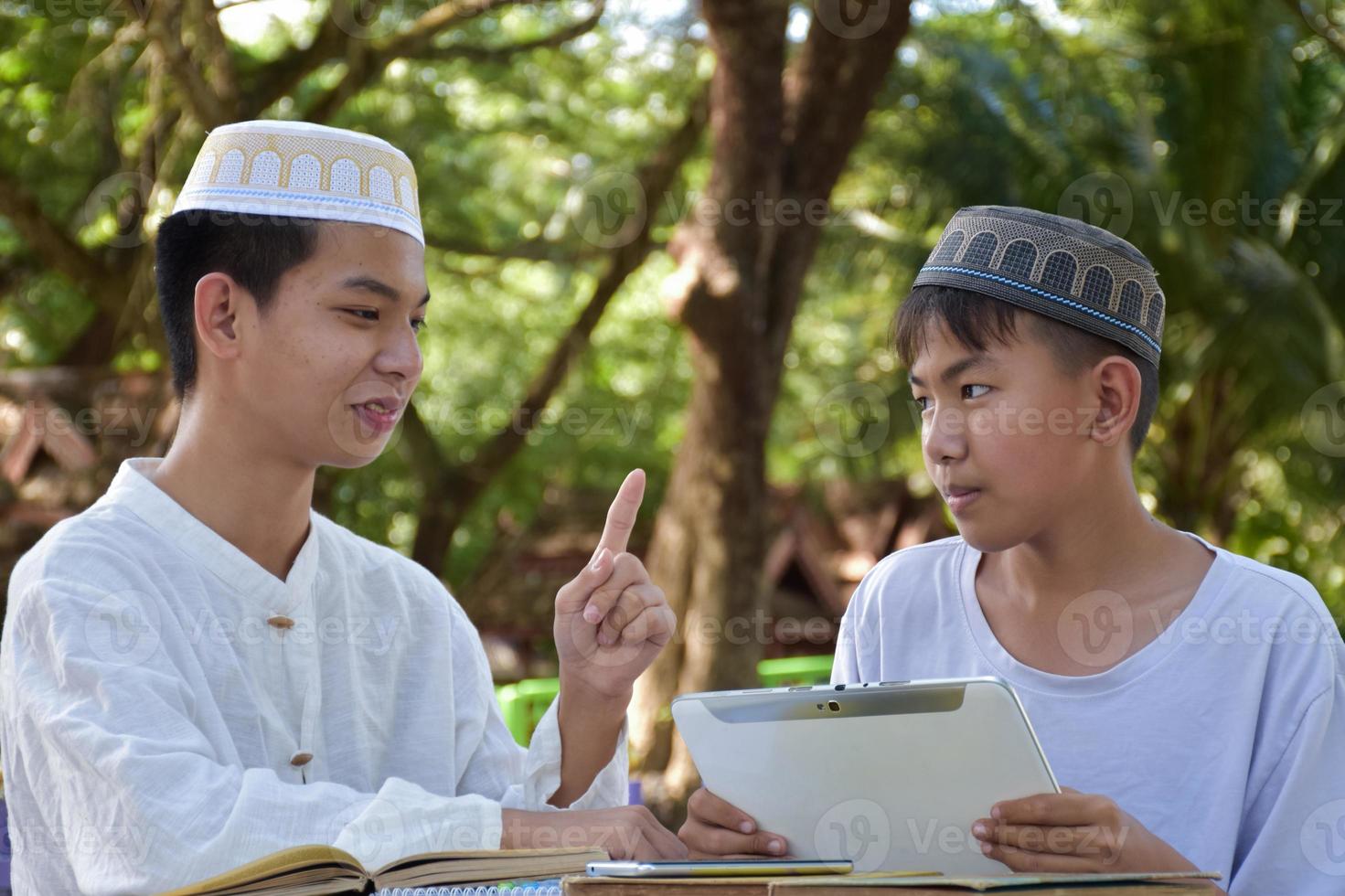 asiatische muslimische jungen sitzen im schulpark zusammen, um zu lesen und ihre täglichen aktivitäten zu lernen und in ihrer freizeit hausaufgaben zu machen, bevor sie nach hause zurückkehren, weicher und selektiver fokus. foto