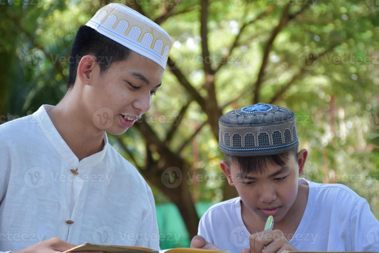 asiatische muslimische jungen sitzen im schulpark zusammen, um zu lesen und ihre täglichen aktivitäten zu lernen und in ihrer freizeit hausaufgaben zu machen, bevor sie nach hause zurückkehren, weicher und selektiver fokus. foto