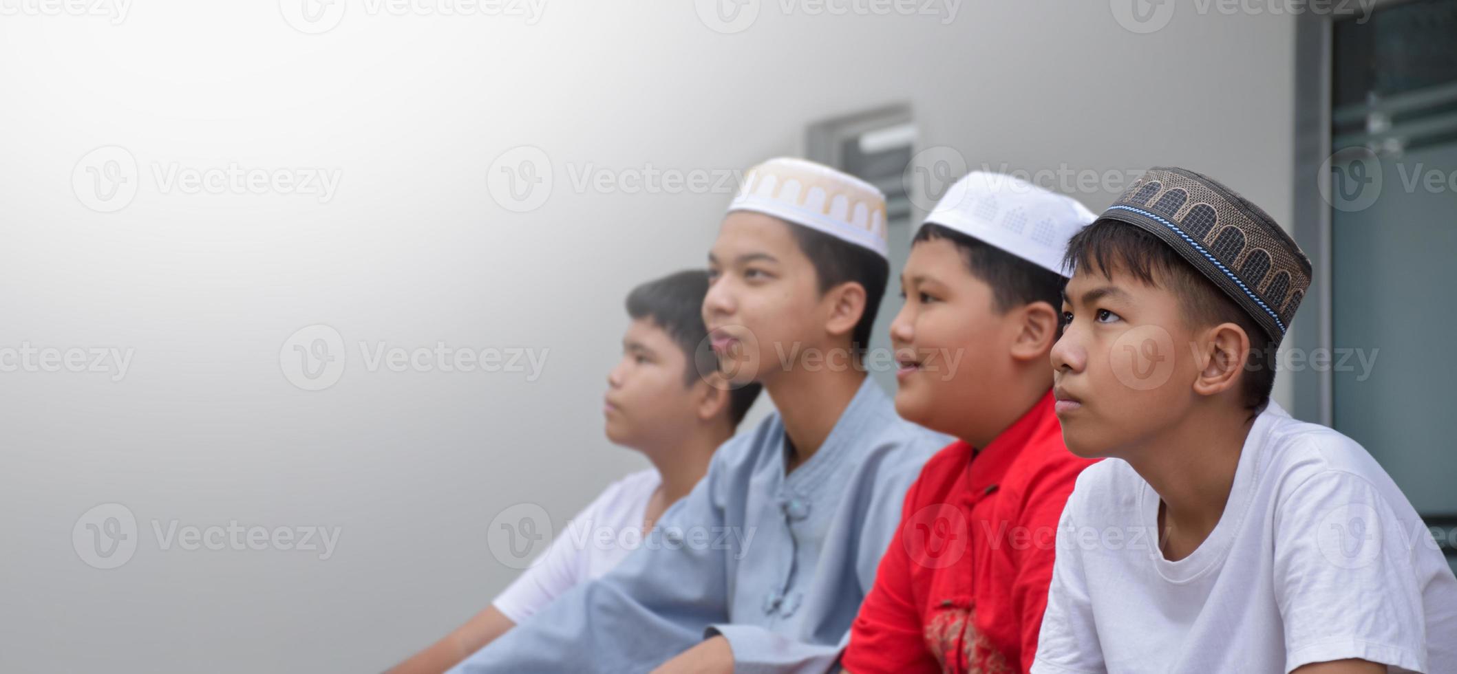 asiatische muslimische oder islamische jungen, die mit muslimischen jungen in einer reihe sitzen, um zu beten oder die religiöse tätigkeit auszuüben, weicher und selektiver fokus. foto