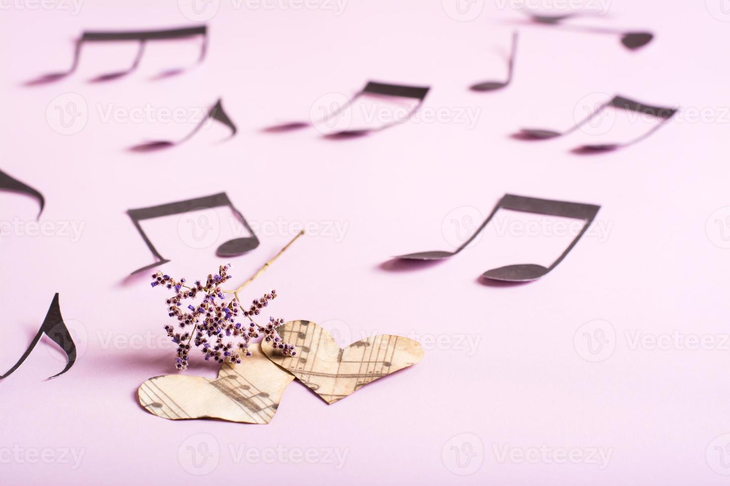 das konzept der liebe zur musik. zwei papierherzen, trockene blumen und notizen herum auf einem rosa hintergrund foto