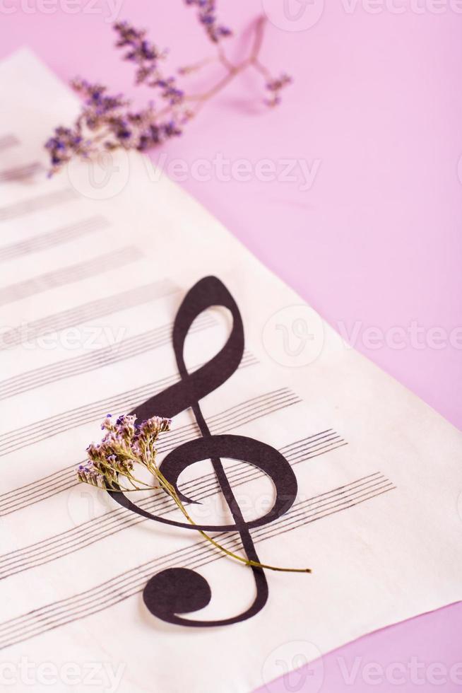 Notenschlüssel aus Papier auf einem Notenblatt und getrockneten Blumen. vertikale Ansicht. foto