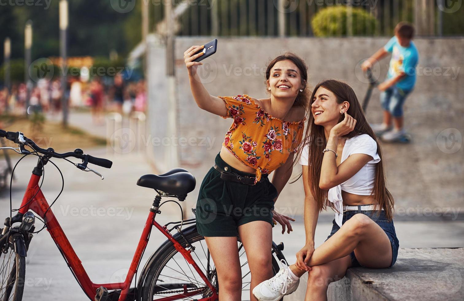 ein Selfie machen. Zwei junge Frauen mit Fahrrad amüsieren sich im Park foto