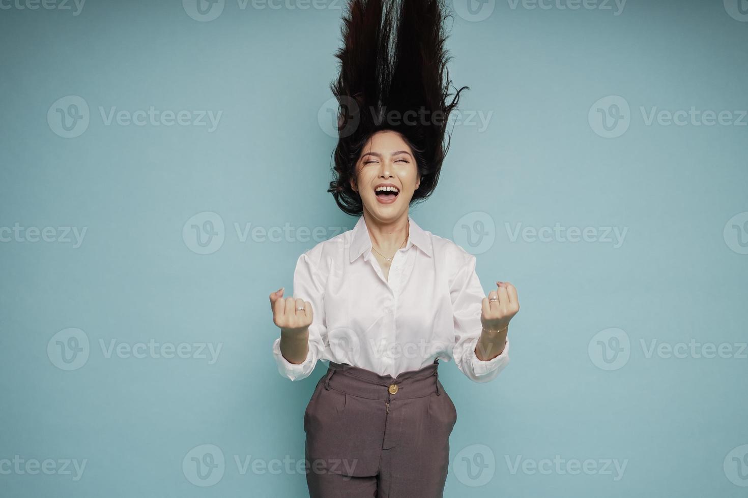 eine junge asiatische Frau mit einem glücklichen, erfolgreichen Ausdruck, der ein weißes Hemd trägt, das durch blauen Hintergrund isoliert ist foto