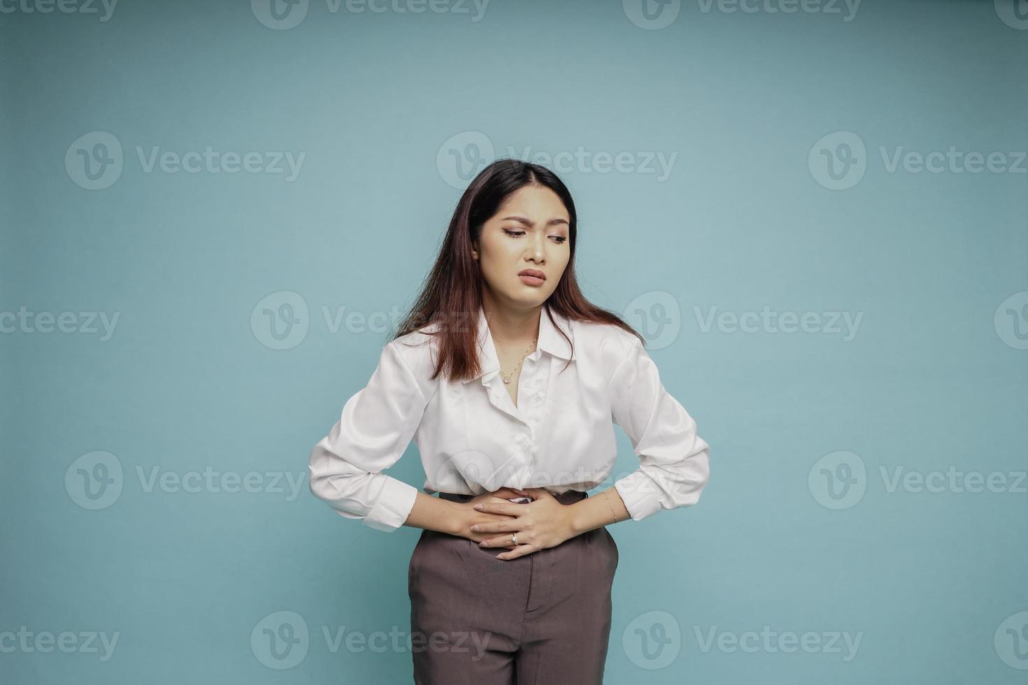 Foto einer jungen unwohl kranken Frau, die die Hand auf dem Bauch hält, leidet unter Schmerzen isoliert auf blauem Hintergrund