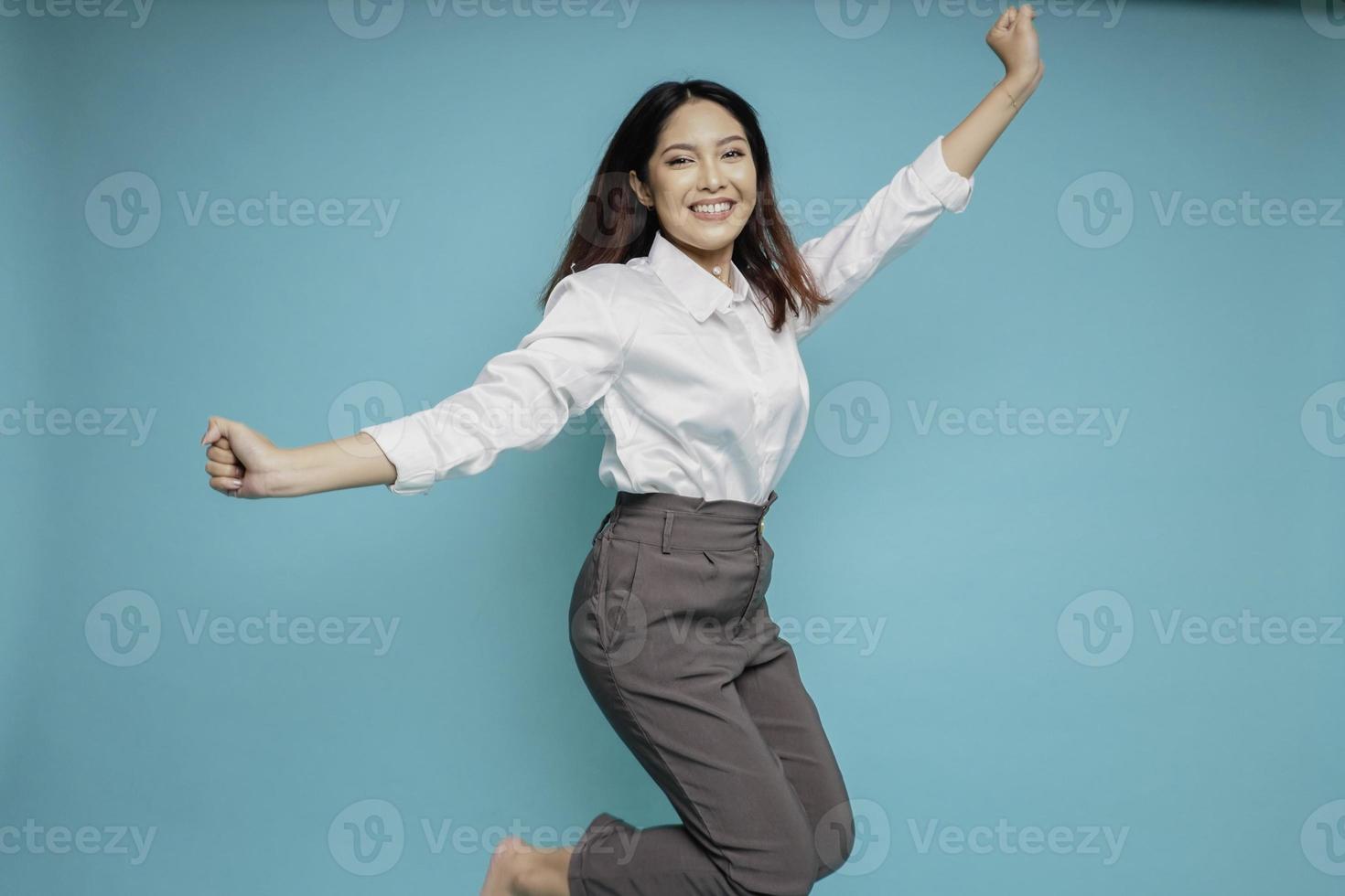 Foto eines aktiven asiatischen Mädchens oder Mitarbeiters, der die Hände hochhebt, trägt ein weißes Hemd, isoliert auf blauem Hintergrund