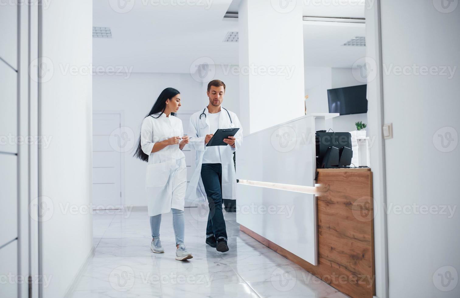 arzt und brünette krankenschwester gehen im krankenhaus spazieren und unterhalten sich bei der arbeit foto