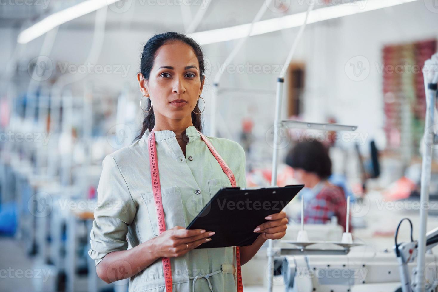 brünette schneiderin arbeitet in der fabrik und hält notizblock in den händen foto