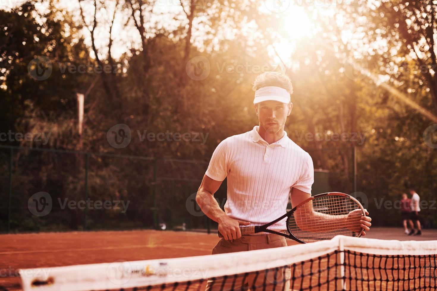 schönes Sonnenlicht. junger tennisspieler in sportlicher kleidung ist draußen auf dem platz foto