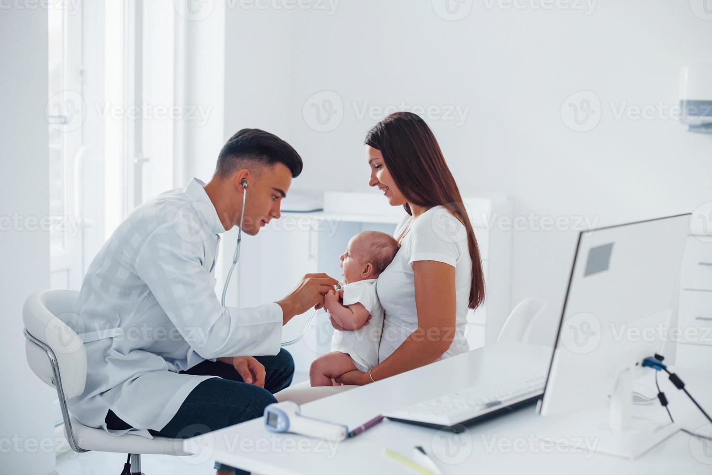 mit Mutters Hilfe. Junge Kinderärztin ist tagsüber mit kleinem Baby in der Klinik foto