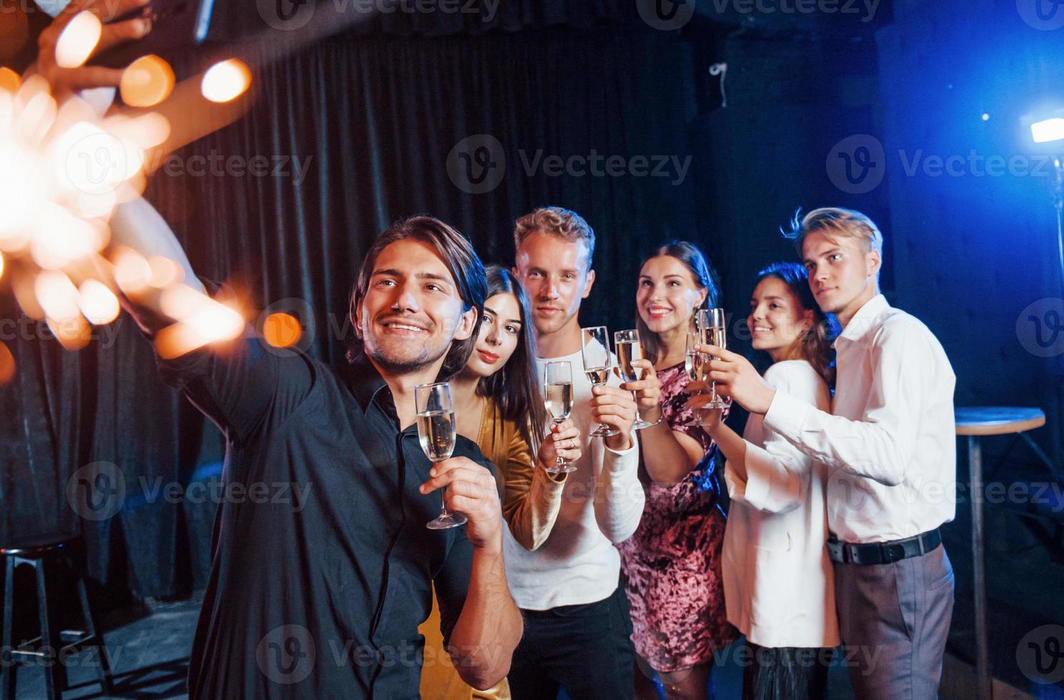 macht ein Selfie. gruppe fröhlicher freunde, die drinnen mit getränken in den händen neujahr feiern foto