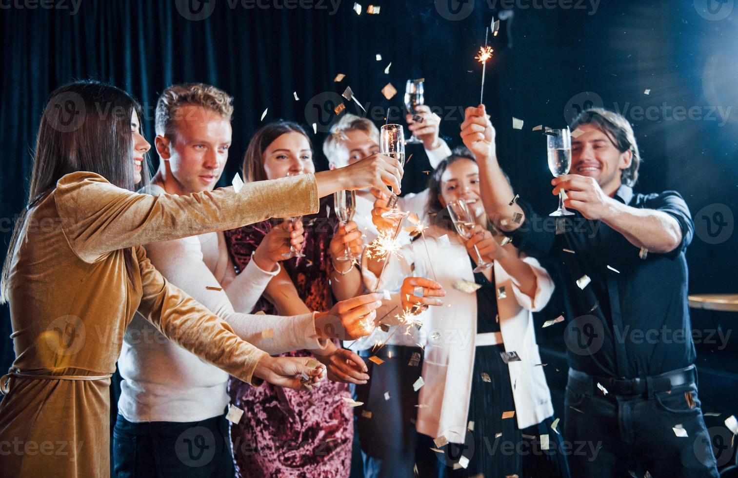 Spaß mit Wunderkerzen. gruppe fröhlicher freunde, die drinnen mit getränken in den händen neujahr feiern foto