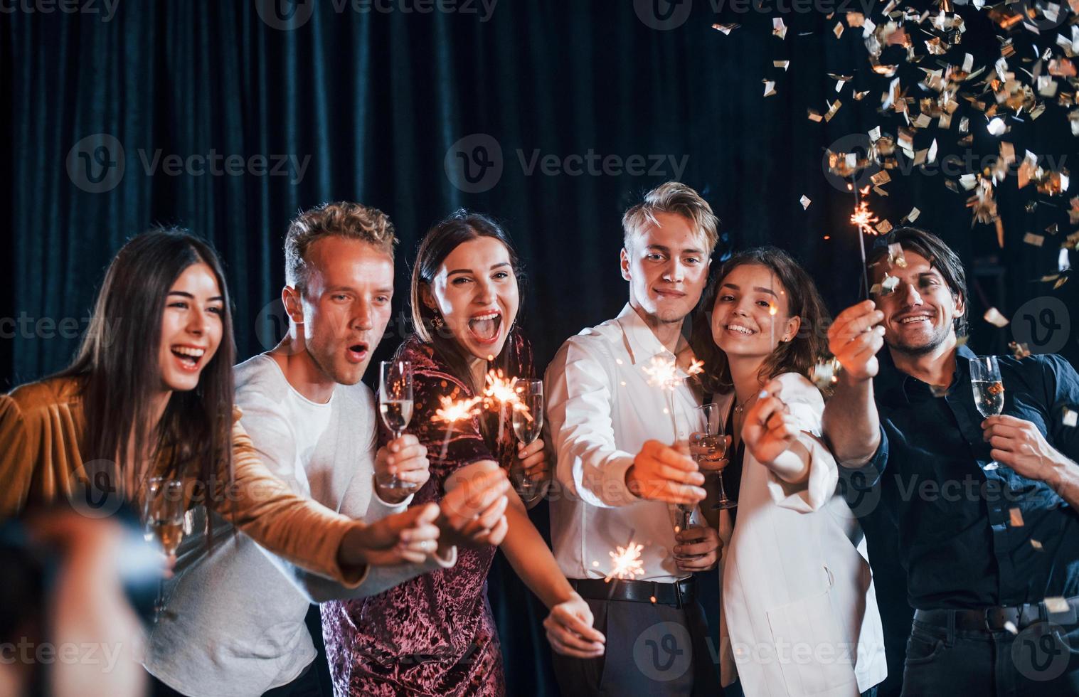 Spaß mit Wunderkerzen. gruppe fröhlicher freunde, die drinnen mit getränken in den händen neujahr feiern foto