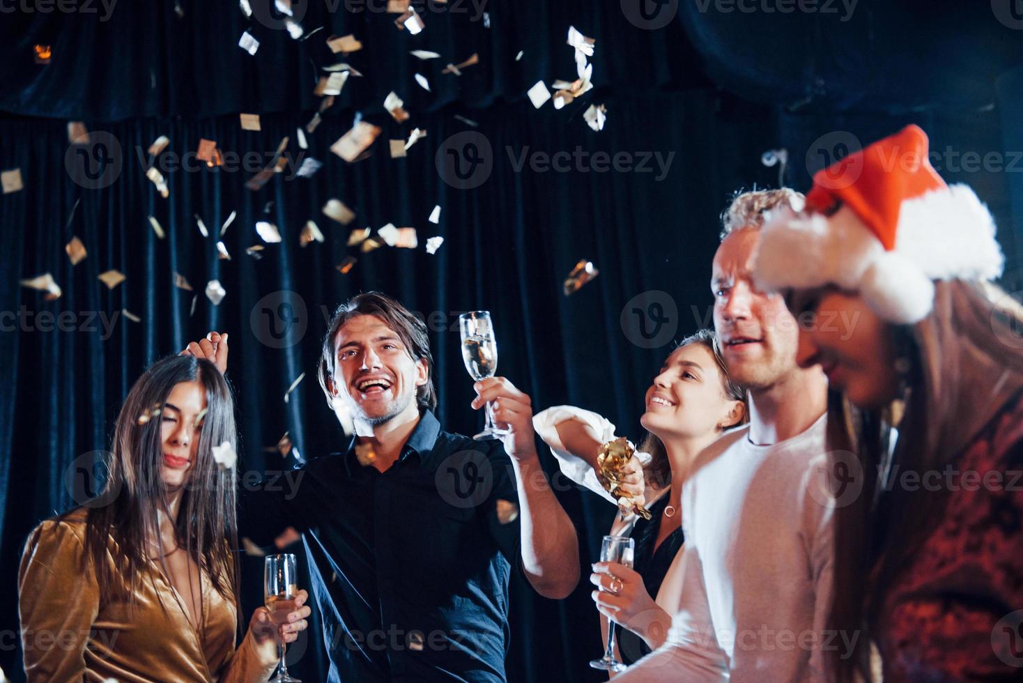 Konfetti liegt in der Luft. gruppe fröhlicher freunde, die drinnen mit getränken in den händen neujahr feiern foto