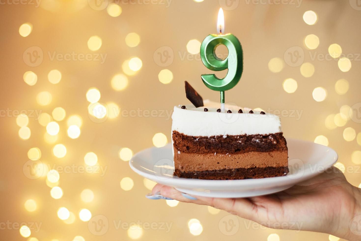 frau, die einen kuchen mit den kerzen der nummer 9 auf festlichem unscharfem bokeh-hintergrund hält foto