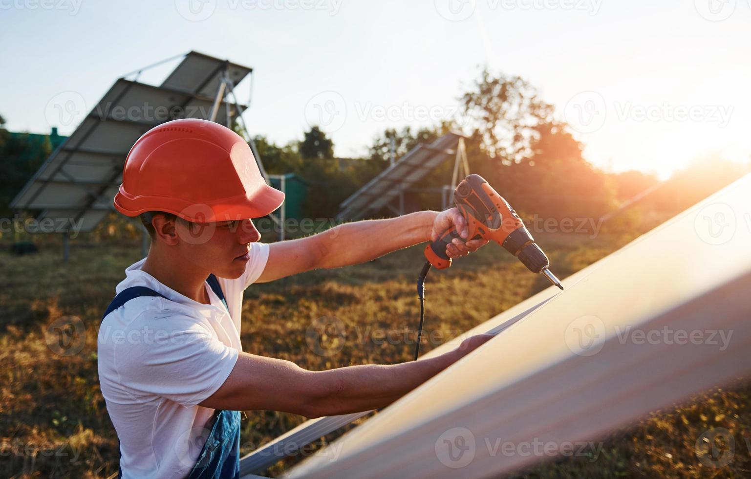 mit Akkuschrauber. männlicher Arbeiter in blauer Uniform im Freien mit Solarbatterien an sonnigen Tagen foto