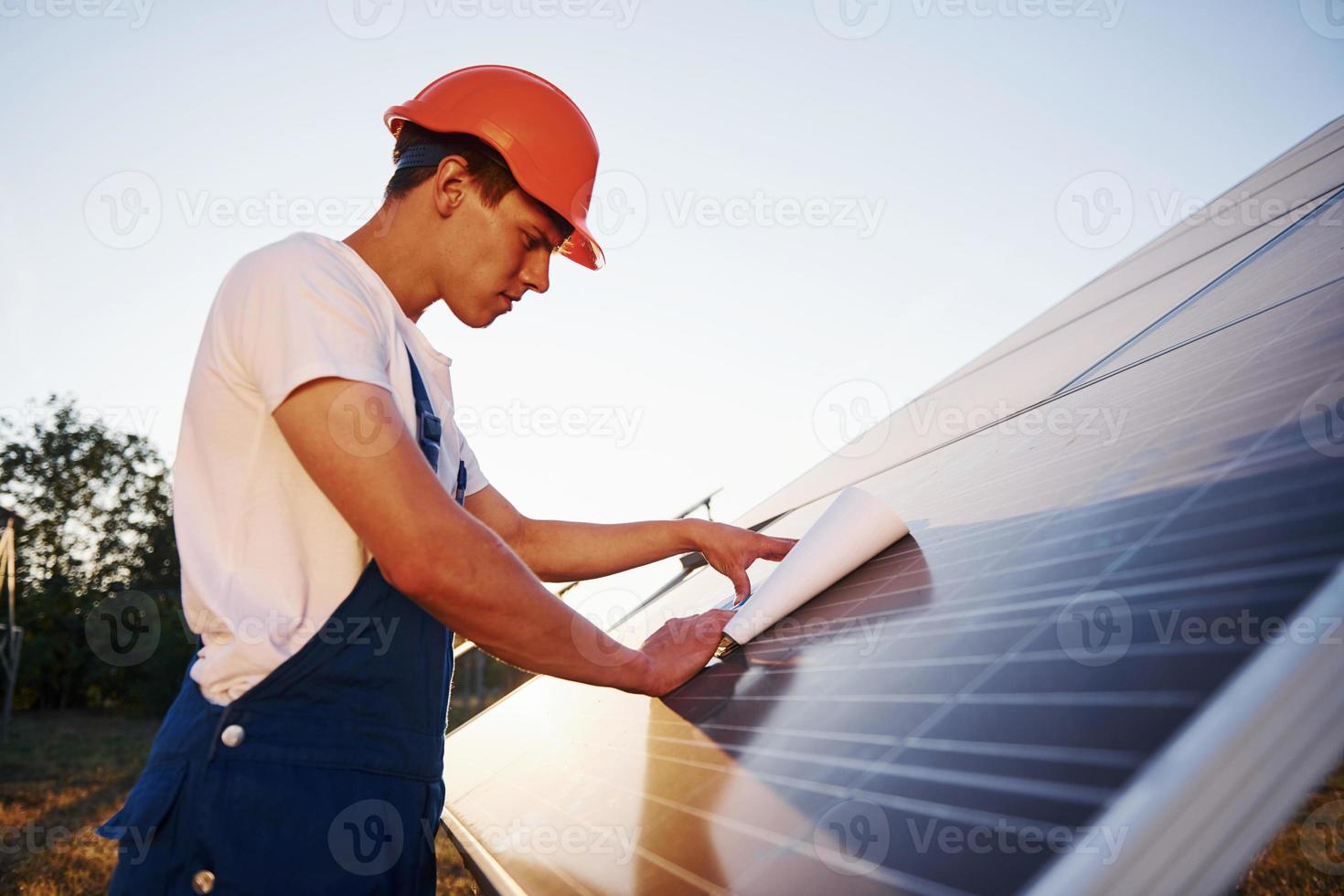 schönes Sonnenlicht. männlicher arbeiter in blauer uniform im freien mit solarbatterien foto