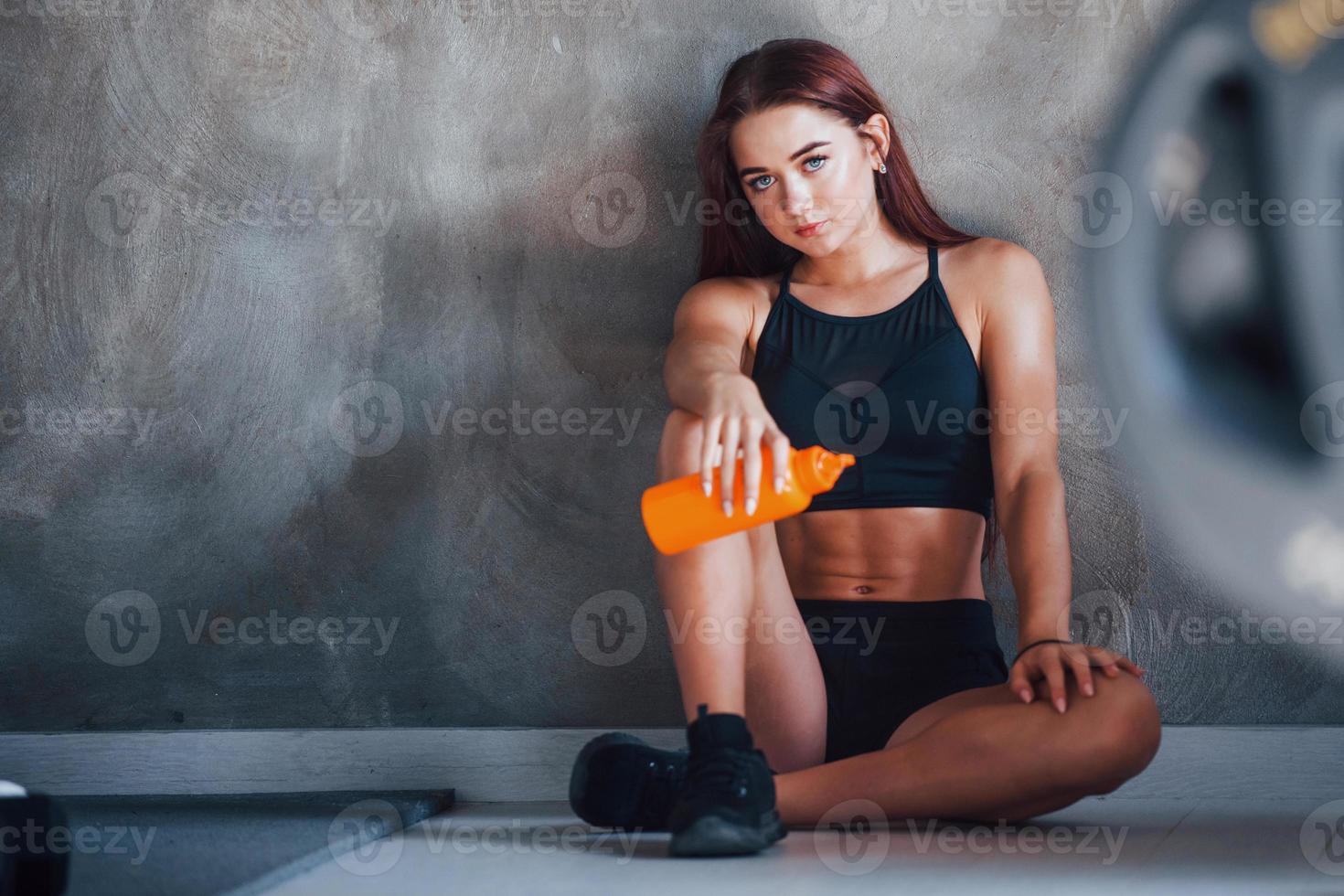 junge fitnessfrau sitzt mit wasser im fitnessstudio auf dem boden foto