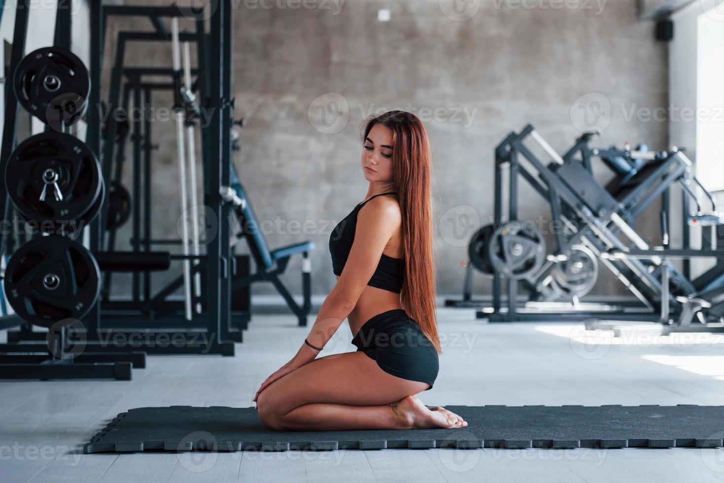 junge Frau mit schlankem Körperbau und in schwarzer sportlicher Kleidung beim Yoga auf der Fitnessmatte foto