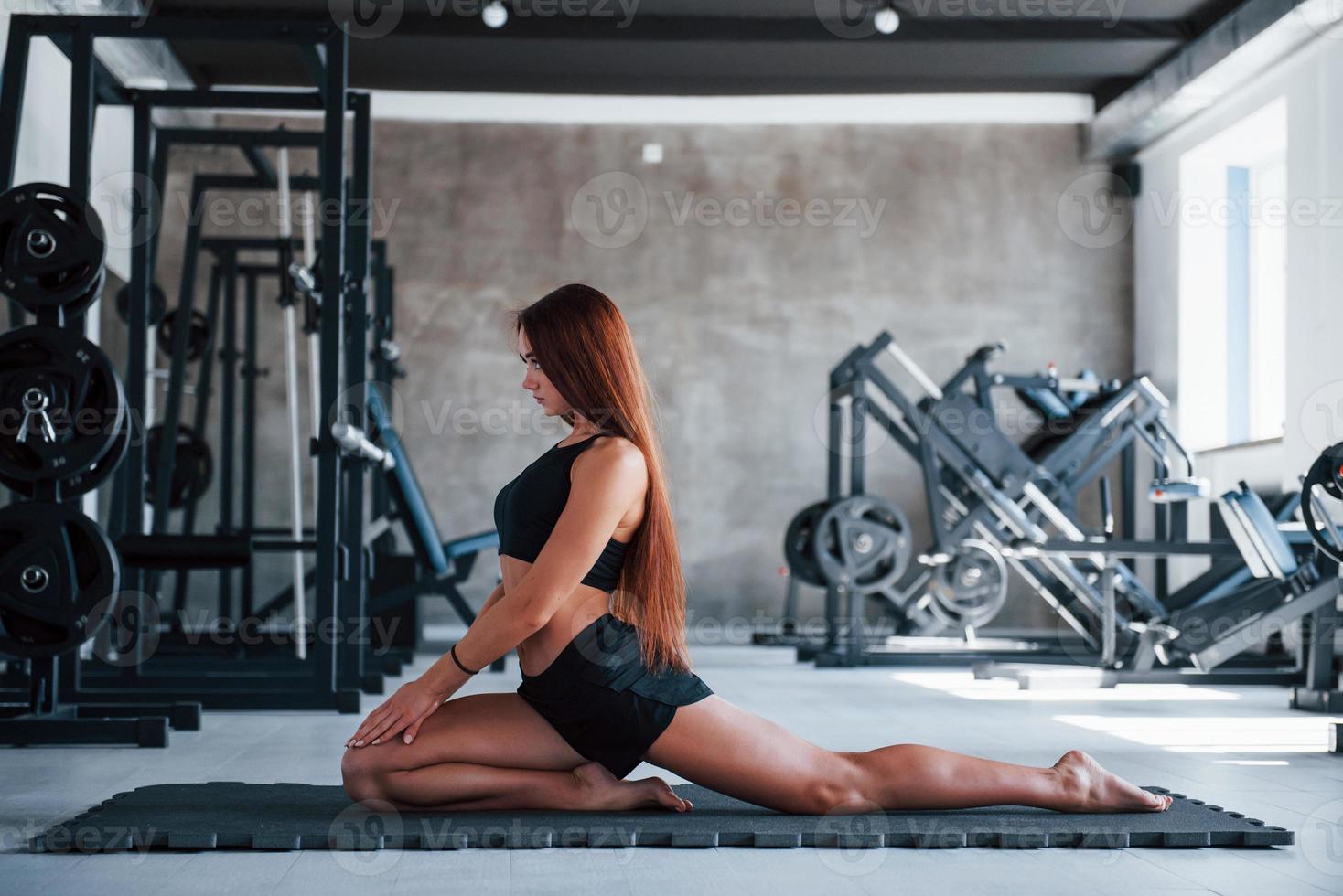 junge Frau mit schlankem Körperbau und in schwarzer sportlicher Kleidung beim Yoga auf der Fitnessmatte foto