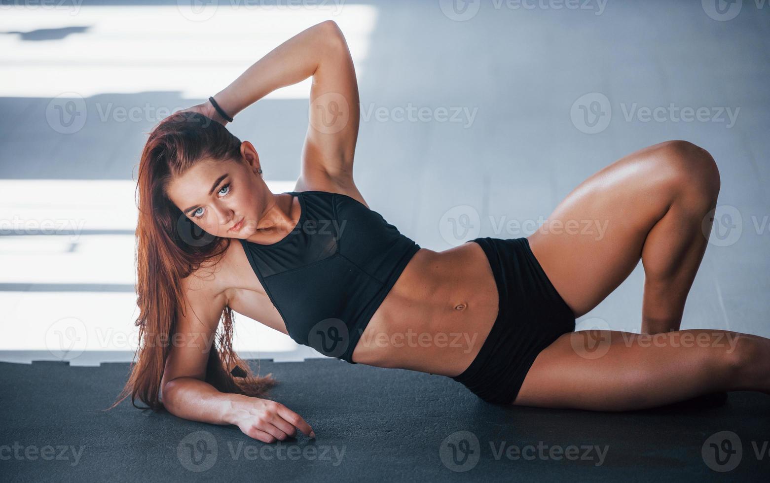 junge Frau mit schlankem Körperbau und in schwarzer sportlicher Kleidung, die sich auf die Fitnessmatte legt foto