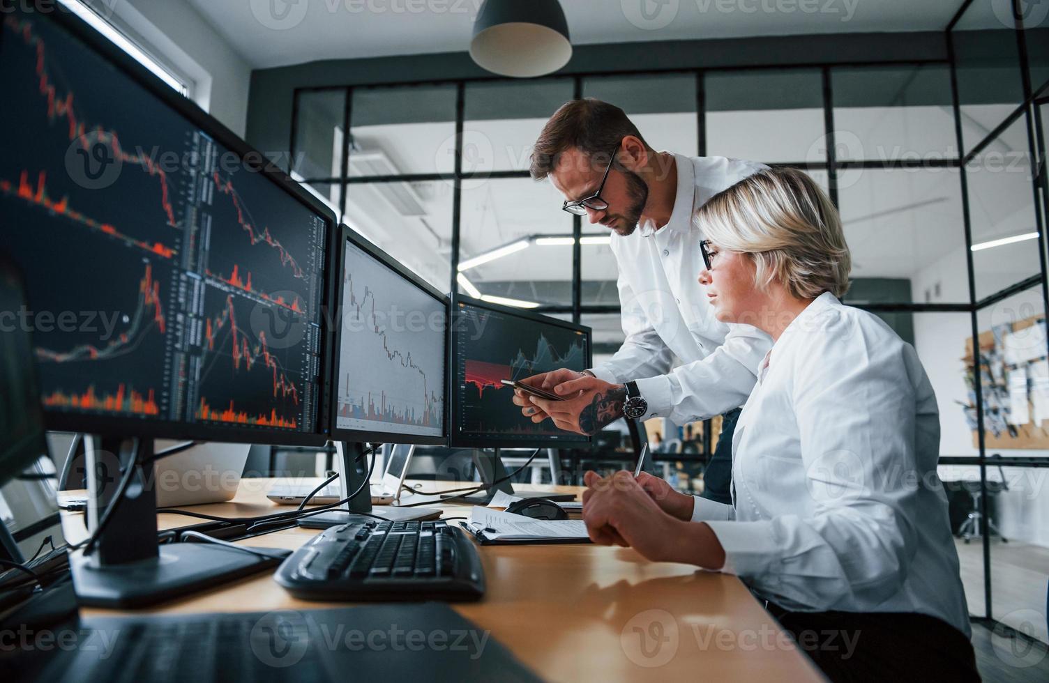 Informationen gemeinsam analysieren. zwei börsenmakler in formeller kleidung arbeiten im büro mit finanzmarkt foto