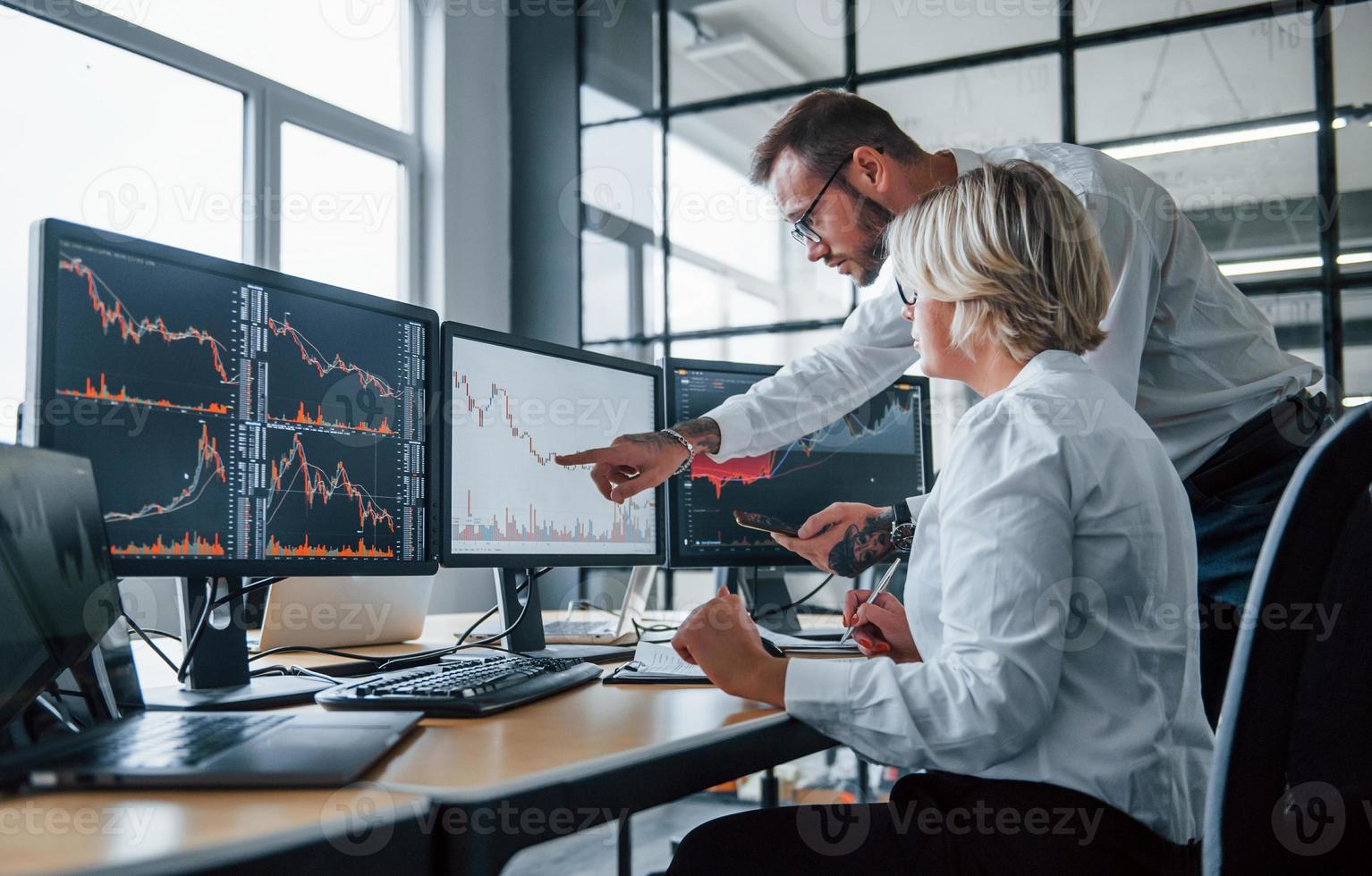 Informationen gemeinsam analysieren. zwei börsenmakler in formeller kleidung arbeiten im büro mit finanzmarkt foto