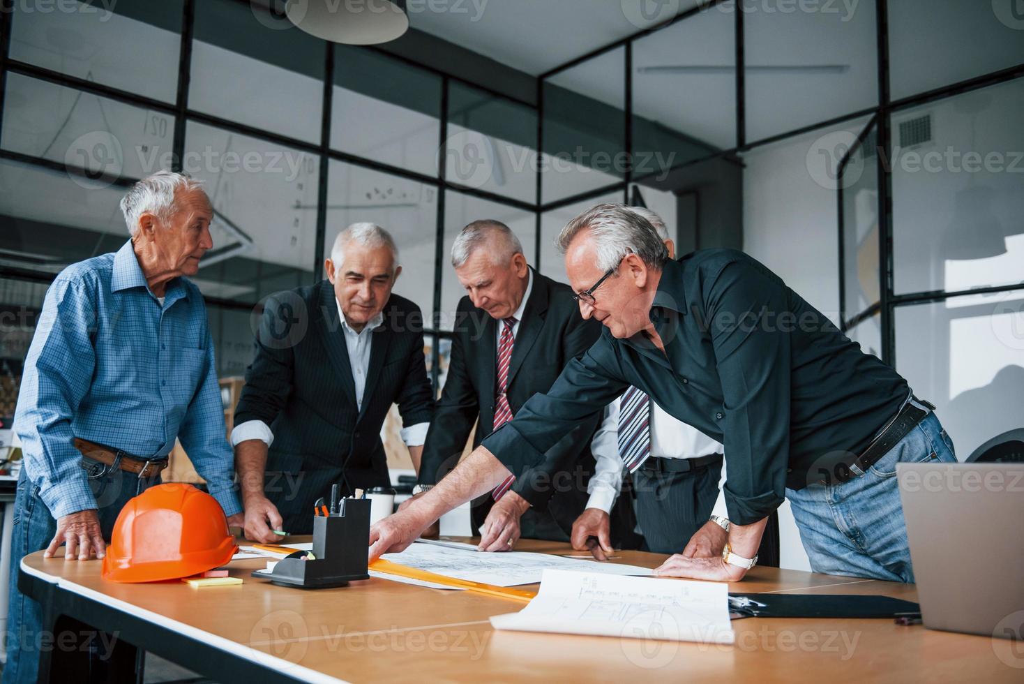 Bauplanung durch Aufmaß auf Papier. Ein älteres Team älterer Geschäftsmannarchitekten trifft sich im Büro foto