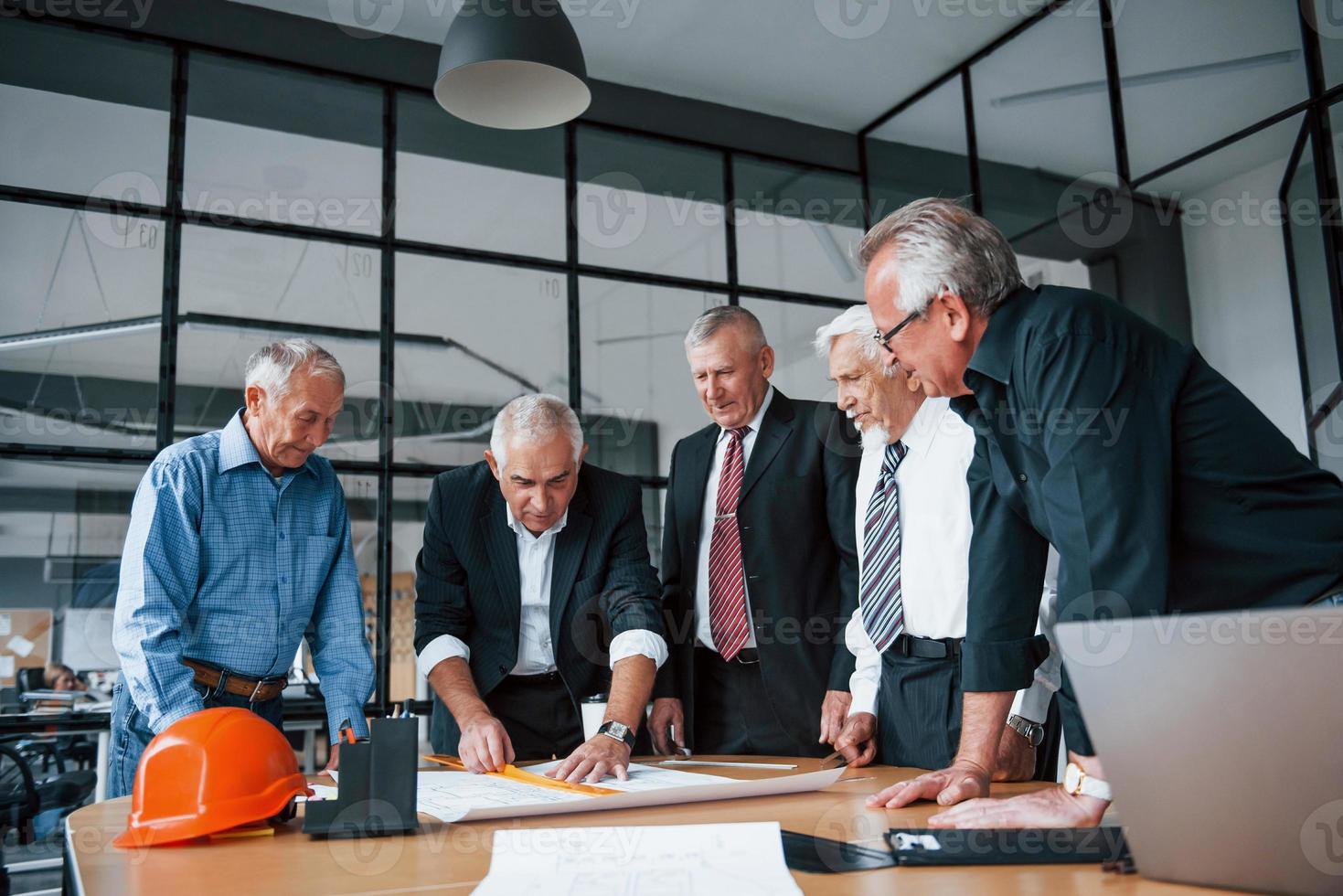 Ein älteres Team älterer Geschäftsmannarchitekten arbeitet mit Plan im Büro foto