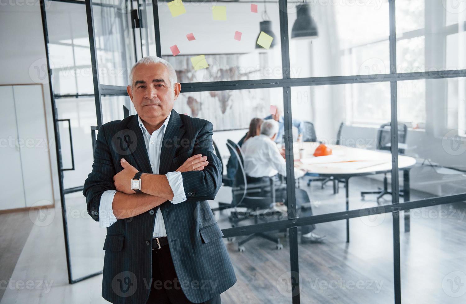 Porträt eines älteren Mannes, der vor einem alten Team älterer Geschäftsmannarchitekten steht, die sich im Büro treffen foto