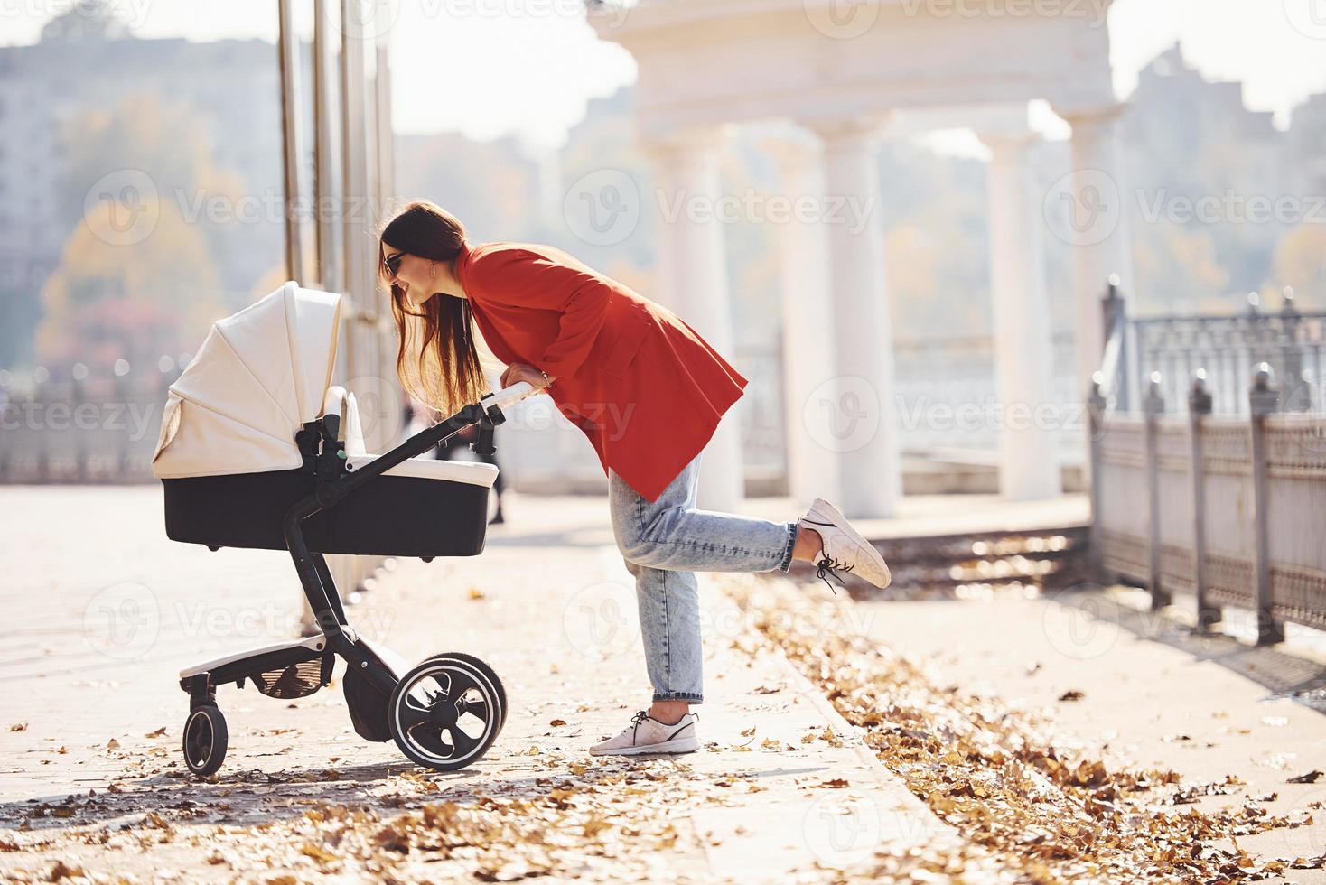 mutter im roten mantel geht zur herbstzeit mit ihrem kind im kinderwagen im park spazieren foto