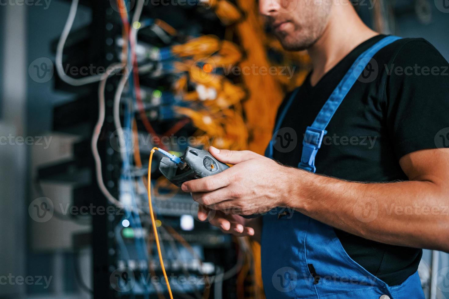 Junger Mann in Uniform hat einen Job mit Internetgeräten und Kabeln im Serverraum foto