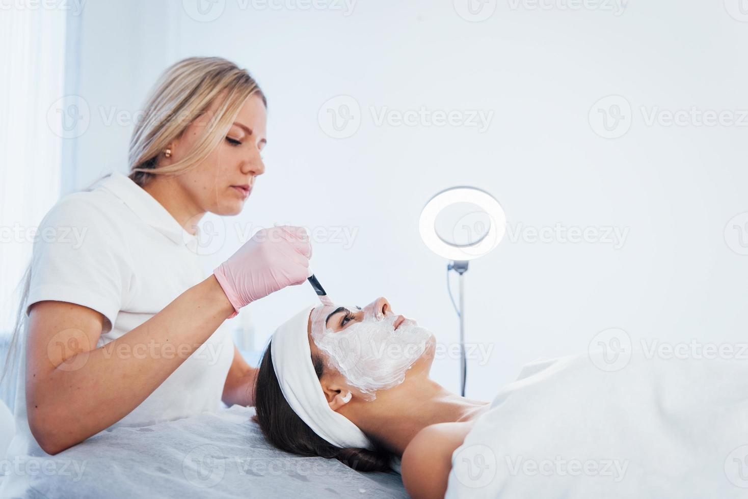 Frau, die sich im Spa-Salon hinlegt und eine Gesichtsreinigung durch eine professionelle Kosmetikerin durchführt foto