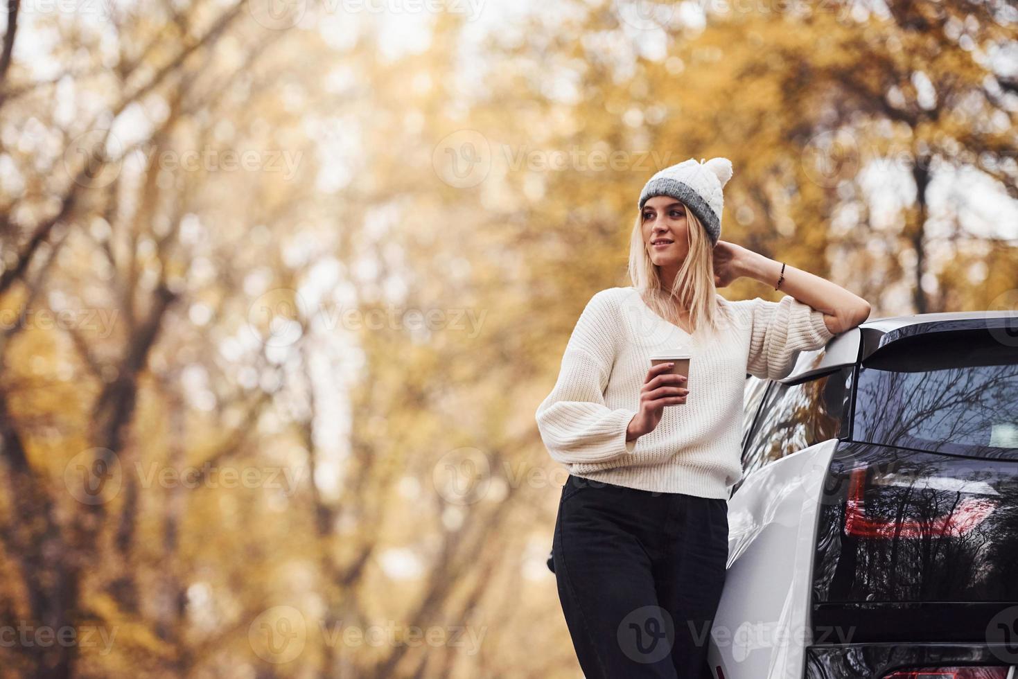 mit Tasse Getränk in den Händen. Mädchen haben Herbstausflug mit dem Auto. modernes, brandneues Auto im Wald foto