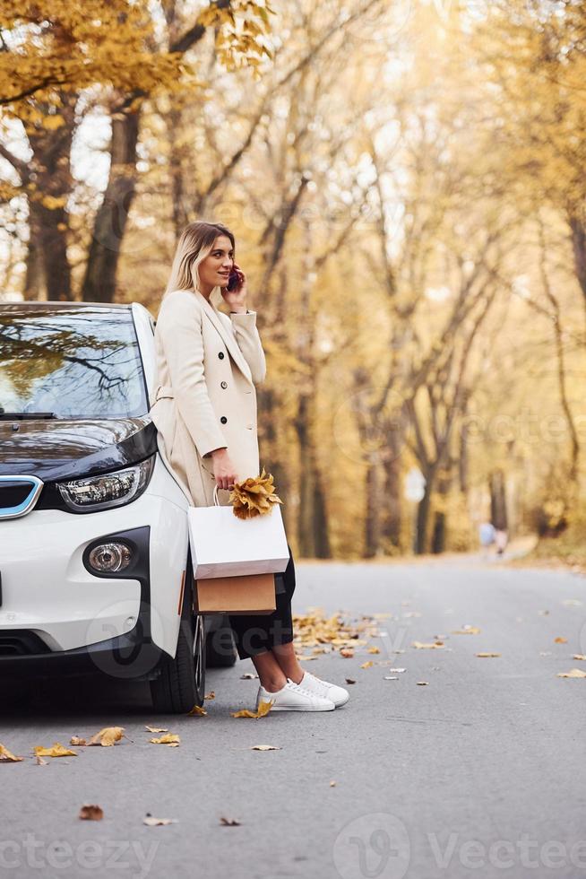 Mädchen haben einen Anruf, wenn sie in der Nähe des Autos stehen. modernes, brandneues Auto im Wald foto