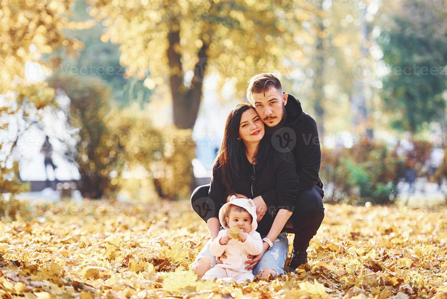 fröhliche familie sitzt auf dem boden und hat spaß zusammen mit ihrem kind im schönen herbstpark foto