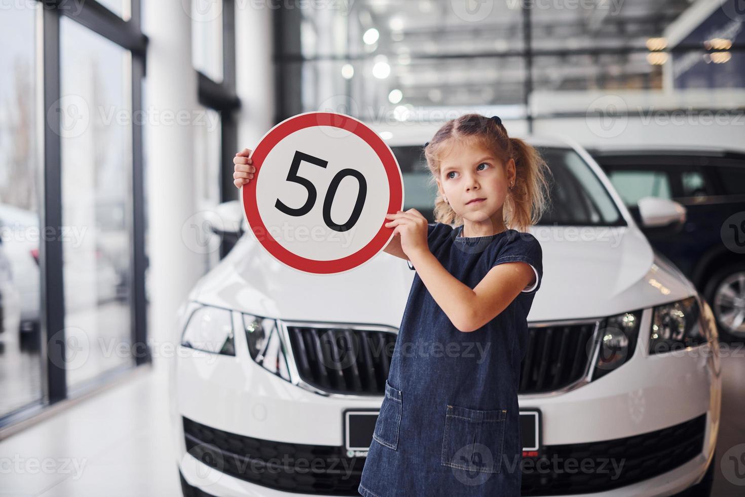 Porträt eines süßen kleinen Mädchens, das im Autosalon ein Straßenschild in den Händen hält foto