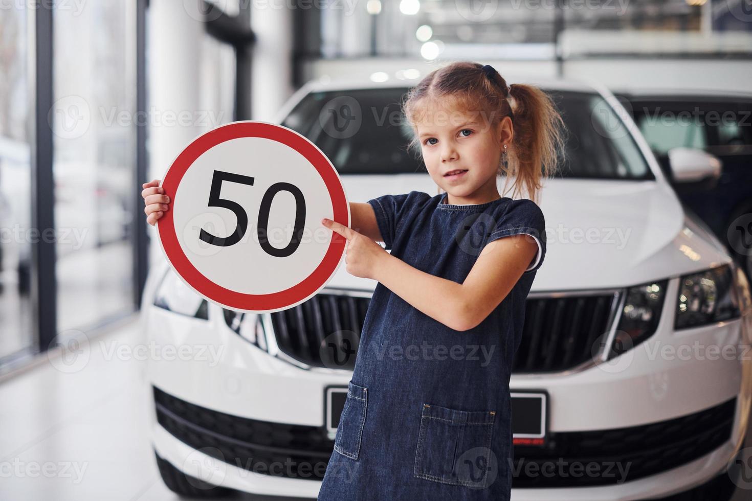 Porträt eines süßen kleinen Mädchens, das im Autosalon ein Straßenschild in den Händen hält foto