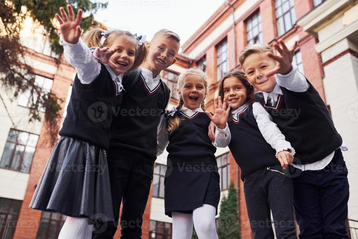 Spaß haben und sich umarmen. Gruppe von Kindern in Schuluniform, die sich im Freien in der Nähe des Bildungsgebäudes befinden foto