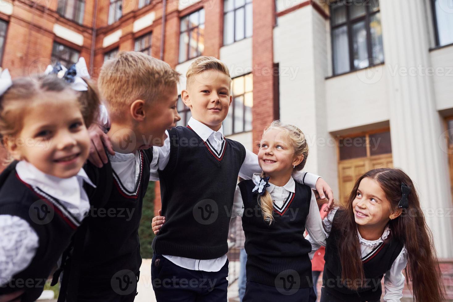 Spaß haben und sich umarmen. Gruppe von Kindern in Schuluniform, die sich im Freien in der Nähe des Bildungsgebäudes befinden foto