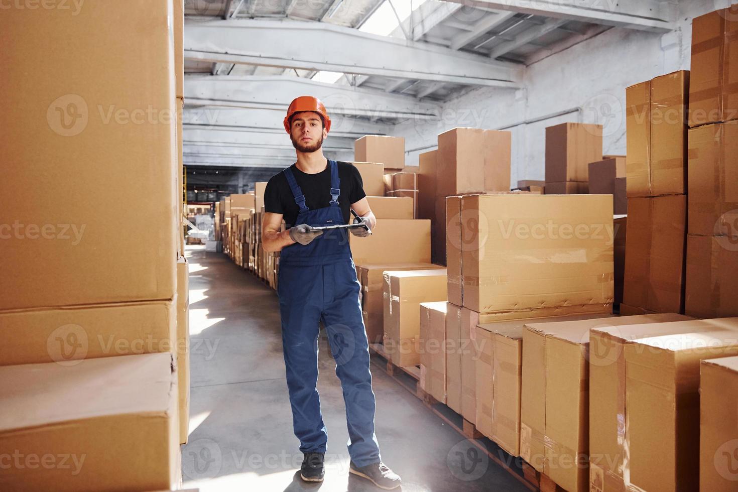 lagerarbeiter in uniform und notizblock in den händen prüft produktion foto