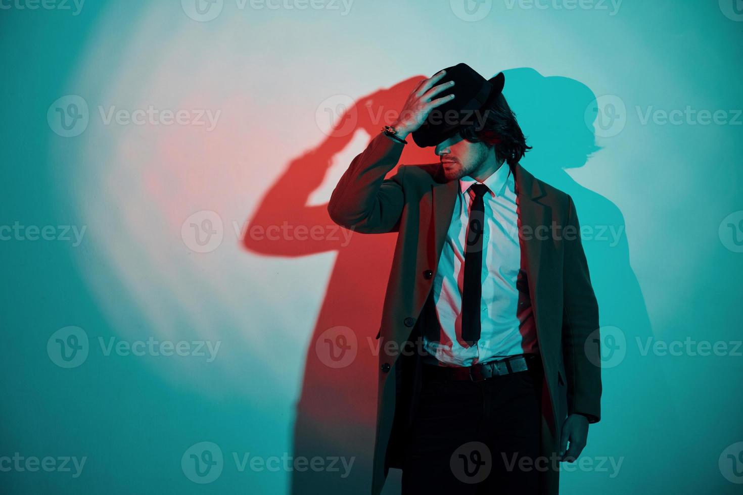 porträt eines jungen, stilvollen mannes in hut, anzug und krawatte, der im studio in neonlichtern steht foto