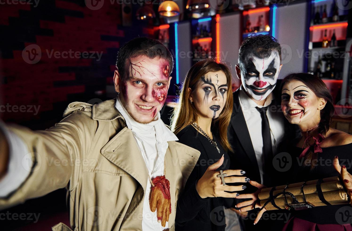 Freunde mit Bombe in den Händen sind auf der thematischen Halloween-Party in gruseligem Make-up und Kostümen foto