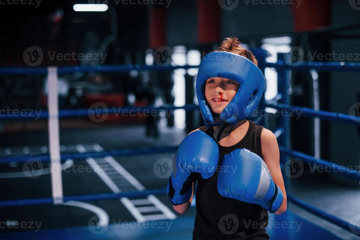 kleiner Junge in Schutzkleidung und mit Nasenblutentraining im Boxring foto