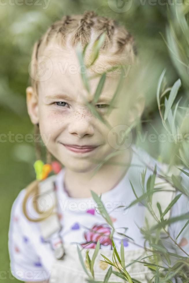 Porträt eines kleinen Mädchens mit Zöpfen durch das Laub. das konzept von sommer und kindheit, emotionen foto