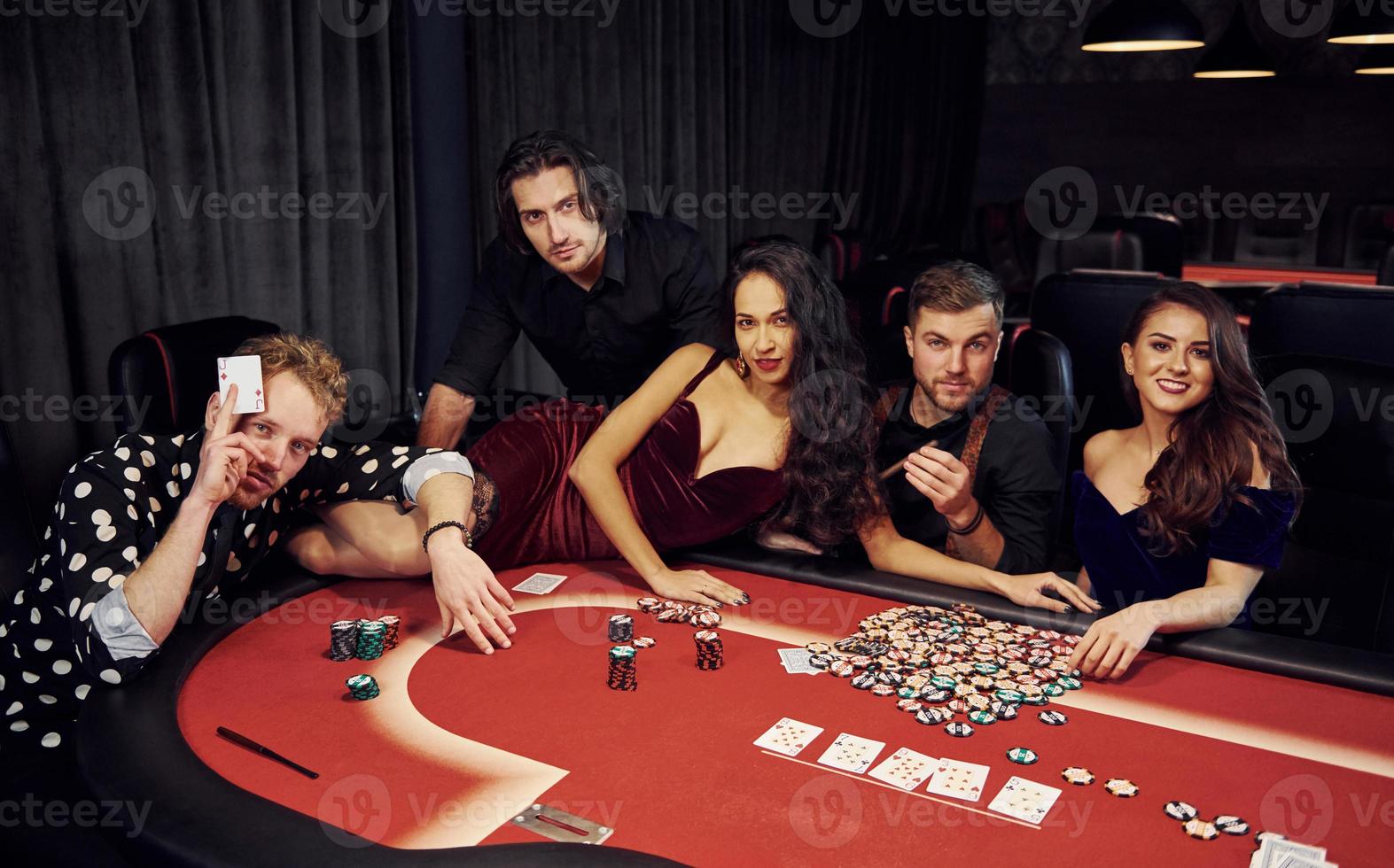 Frau, die sich auf den Tisch legt. Gruppe eleganter junger Leute, die zusammen im Casino Poker spielen foto