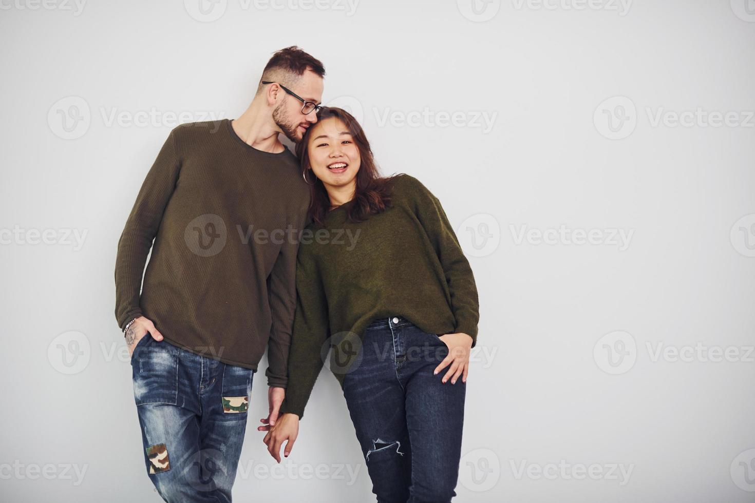 glückliches multiethnisches Paar in Freizeitkleidung ist drinnen im Studio zusammen. Kaukasier mit asiatischer Freundin foto